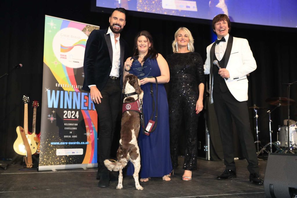 Alex accepts her award from TV presenter Rylan Clark, with Hearing dog Otto and two other hosts.
